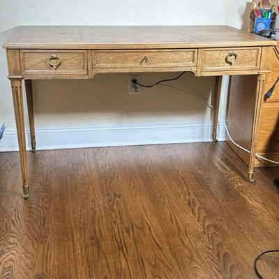 BAKER FURNITURE DESK | Wood desk having 3 split width drawers with brass pulls over fluted legs with brass casters, marked “Milling Road...