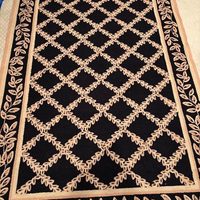 Black area rug with a tan vine lattice pattern.