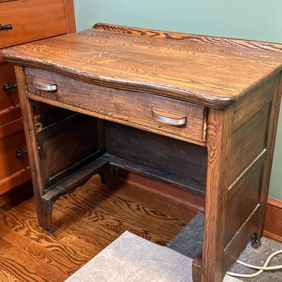 Small Single Drawer Desk | Vintage wooden desk with a single drawer featuring two pull handles, set on caster wheels and possibly once...