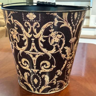 Decorative Metal Bucket | Decorative metal bucket with a curved handle, featuring gold floral and scroll motifs against a dark background...