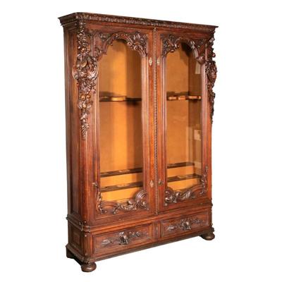 MONUMENTAL ANTIQUE BLACK FOREST CARVED GUN CABINET | Probably late 19th century, having a flat top with sculpted moulding over two glazed...