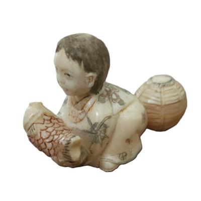 Sale Photo Thumbnail #32: Antique Japanese carved netsuke of a seated man with a fish and basket. Artist signed. With Himotoshi (two holes) used for the cord to attach the Netsuke to the obi. Measures 2 1/2".