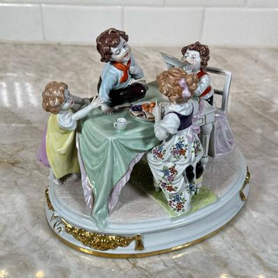 German Porcelain Figural Group | German porcelain figural group depicting children sitting around a table. Features gilt rococo-style...