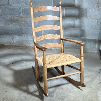 Ladder Back Rocking Chair With Rush Seat | A large rocking chair with a light colored wood frame having shaped horizontal slots, turned...