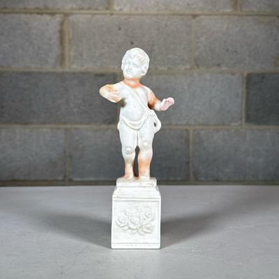 Porcelain Putti Figure | Designed as a putti standing on a floral decorated pedestal; no apparent markings Dimensions: h. 6.75 in
