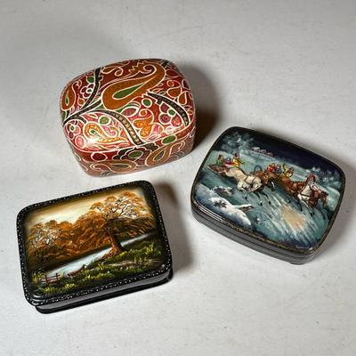 (3pc) Russian Lacquered Boxes | Including one with a sleigh riding scene and one depicting a riverside landscape, both signed in the...