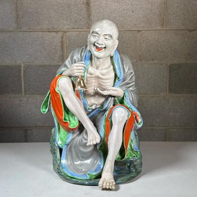 Chinese Porcelain Elder Figure | A laughing Luohan (or Buddhist immortal) seated and holding a bell, with colorful glaze and detailing to...