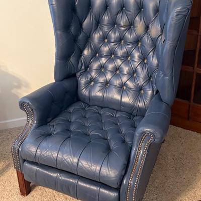 Tufted blue leather wingback chair, appears vintage, with nailhead trim and wood legs.
