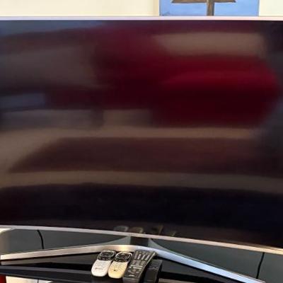 Flat-screen television, appears modern LED TV with curved screen; remote controls shown.