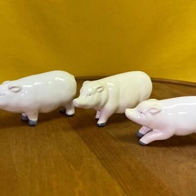 A set of three white ceramic pig figurines with grey hooves