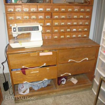 ANTIQUE OAK HARDWARE STORE CABINET PACKED FULL OF SEWING NOTIONS, YARDAGE AND CRAFT ITEMS. ALSO HAVE A WORKING NEWER SIN